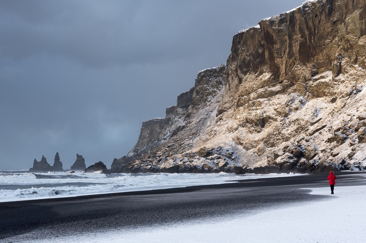 Een reiziger op het zwarte strand van Vik in Zuid IJsland, met de Reynisdrangar op de achtergrond.