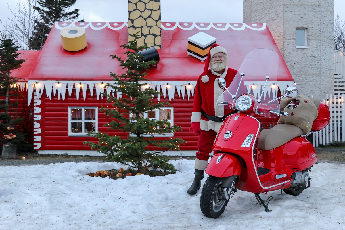 De kerstman staat met een scooter voor het kersthuis in Akureyri, Noord IJsland.