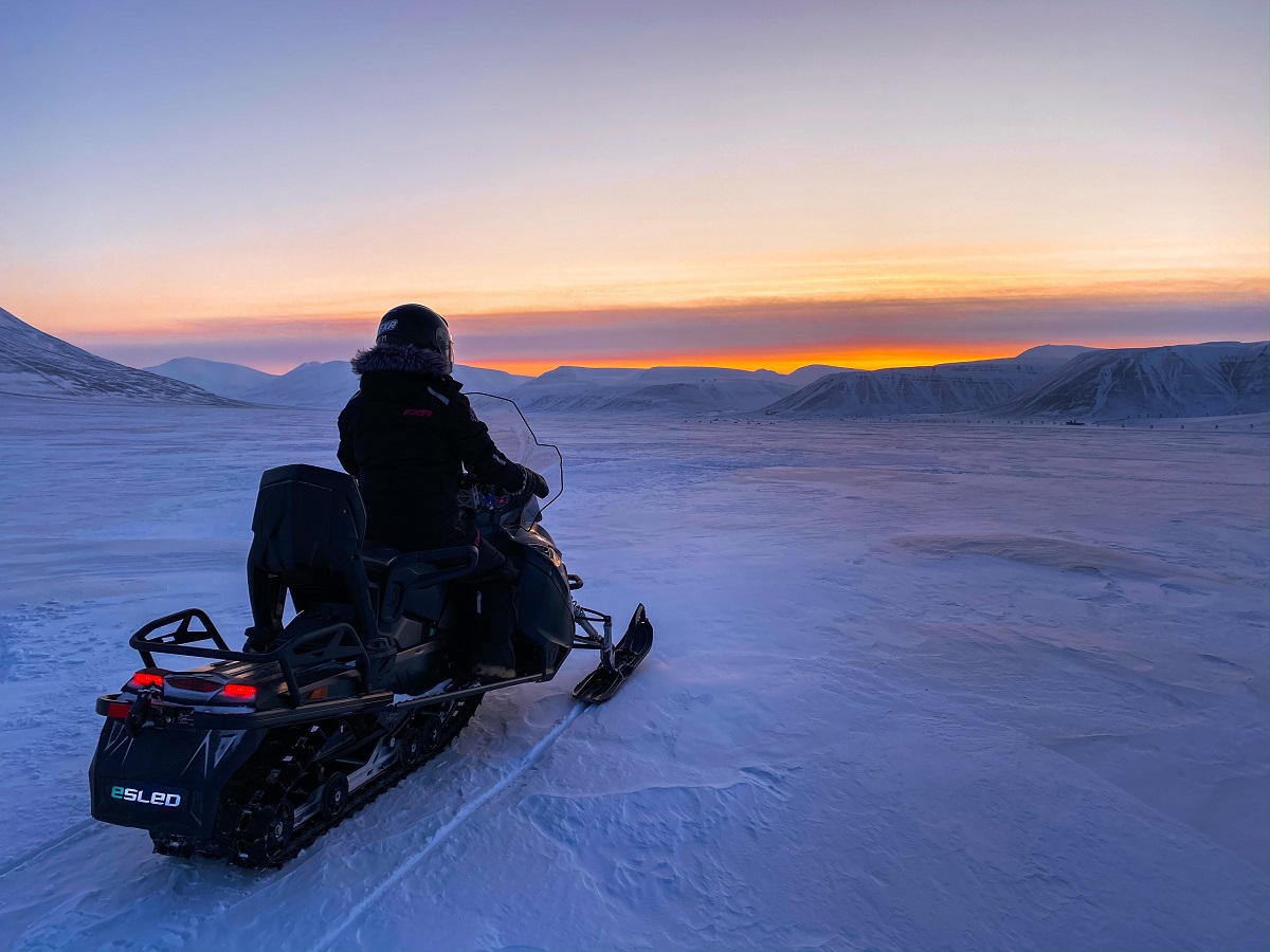 Een reiziger op een sneeuwscooter tijdens zonsondergang in Spitsbergen.