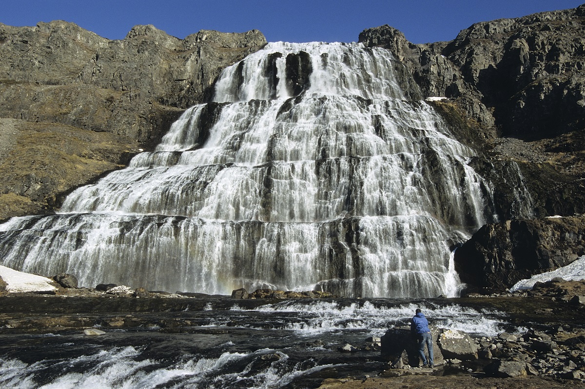 Een toerist op de Westfjorden in IJsland bewondert de mooie Dynjandi waterval die in zeven trappen naar beneden valt.