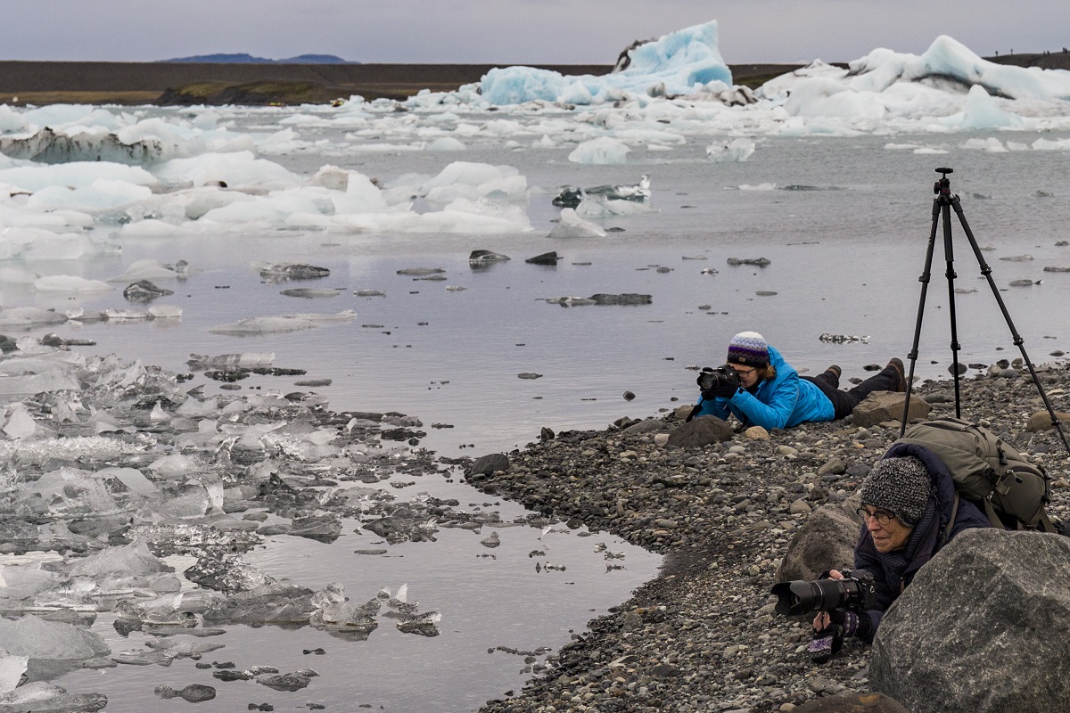 Liggend fotograferen twee reizigers de ijsschoten in het ijsbergenmeer bij Jokulsarlon in Zuidoost-IJsland.