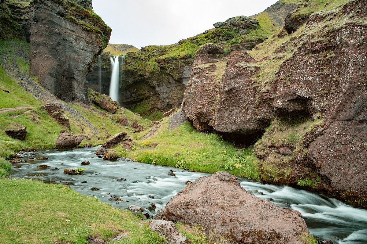 In de verte zie je in het groene landschap de waterval Kvernufoss.