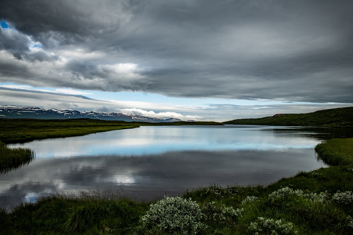 De donkere wolken weerspiegelen in het water van het stille meer.
