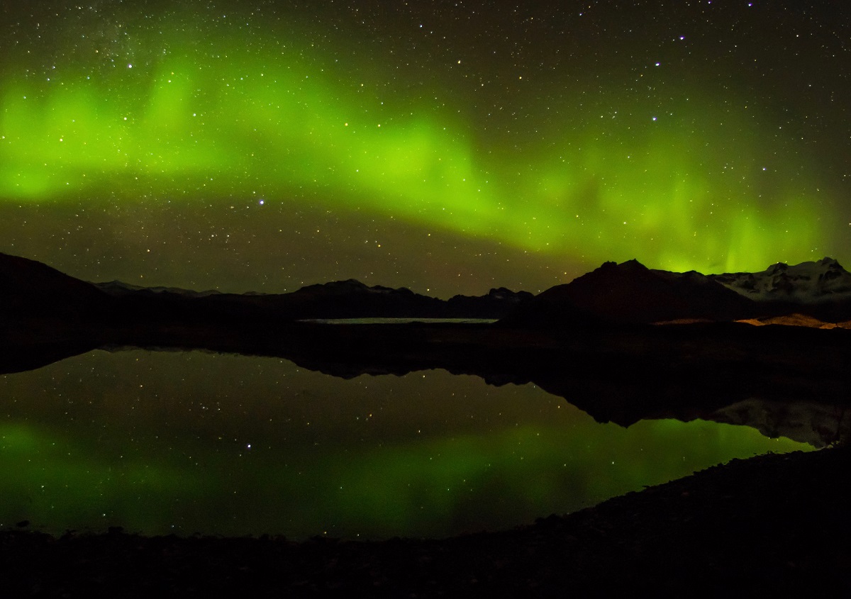 Het groene noorderlicht weerspiegelt in het meer.