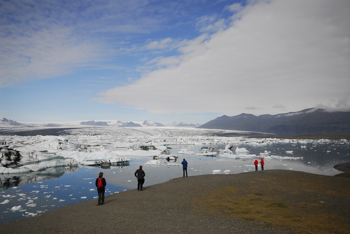 Reizigers kijken in IJsland naar de ijsbergen in het ijsbergenmeer en de gletsjer in de verte.