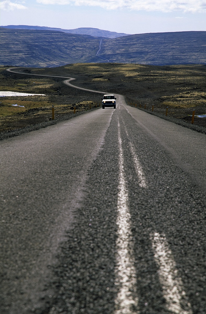 Een auto op een rustige weg door het bergachtige landschap van IJsland.