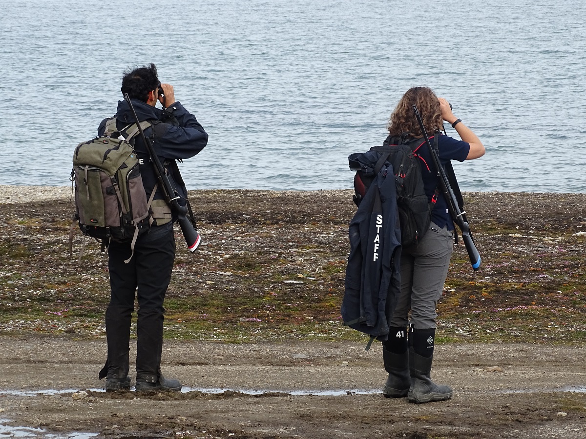 Gewapende gidsen speuren de omgeving af met verrekijkers tijdens wandeling op Spitsbergen.