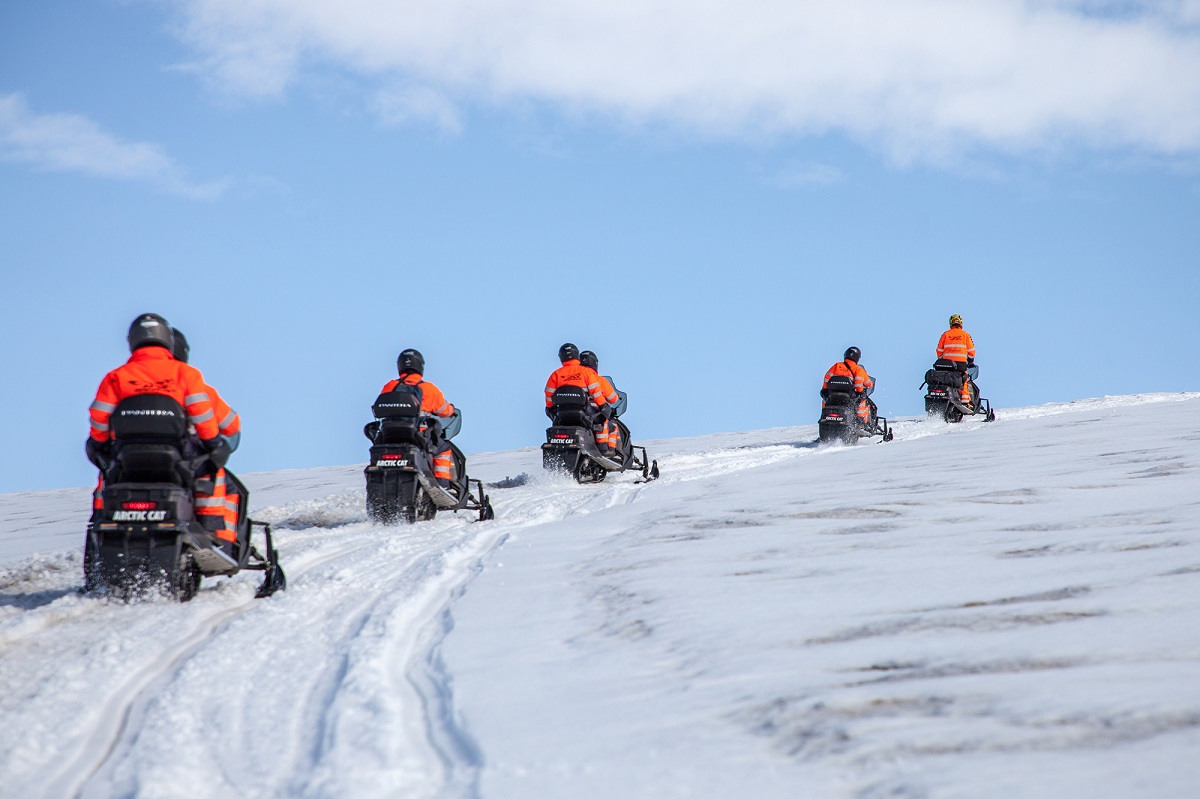 Een groep reizigers op sneeuwscooters die rijden over de Solheimajokull gletsjer in IJsland in oranje thermopak.