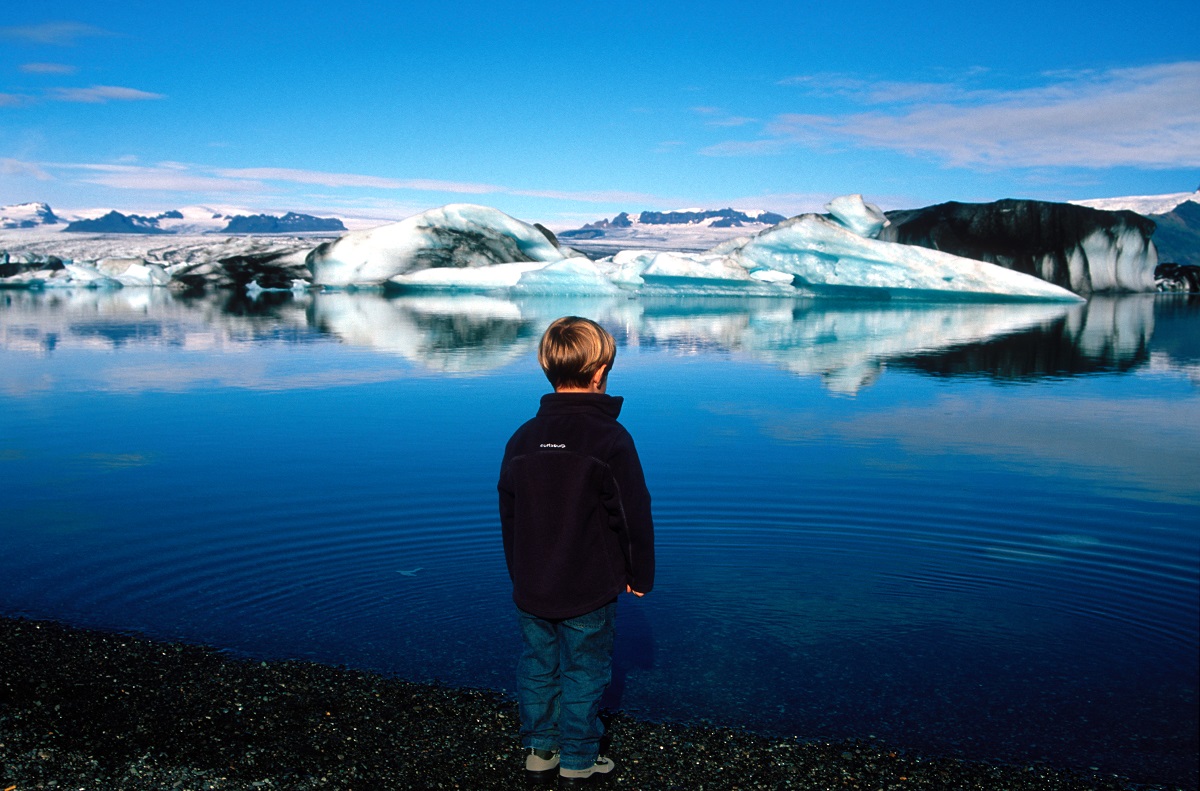 Kind staat te genieten bij het blauwe water van het ijsbergenmeer Jokulsarlon, in zuidoost IJsland.