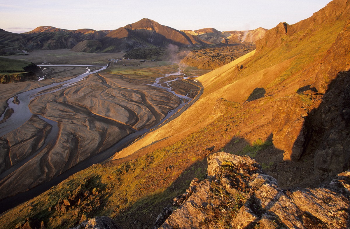 Zonsondergang in Landmannalaugar, de hooglanden van IJsland, met bergen en rivierbedding in oranje zonlicht.