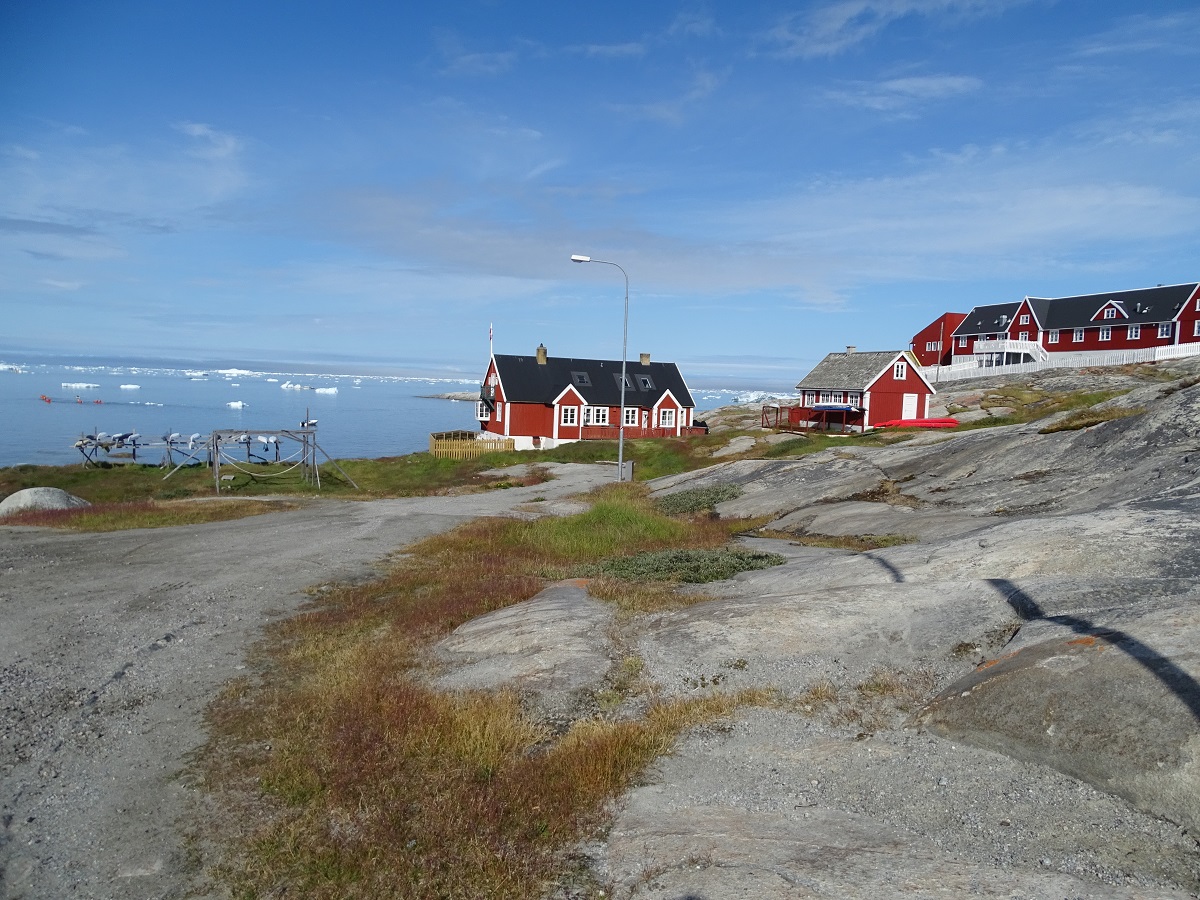 Rode, houten huisjes in de baai van Ilulissat, west Groenland, met uitzicht op drijvende ijsbergen.