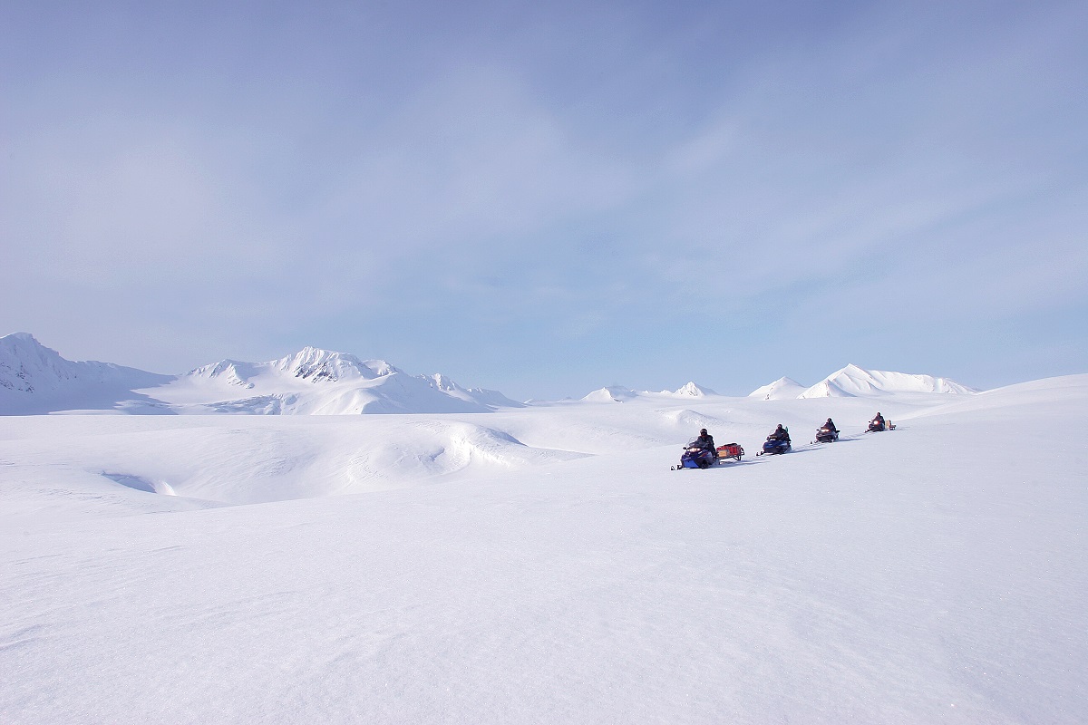 Een groepje sneeuwscooters op de gletsjer op Spitsbergen in een wit sneeuw landschap.