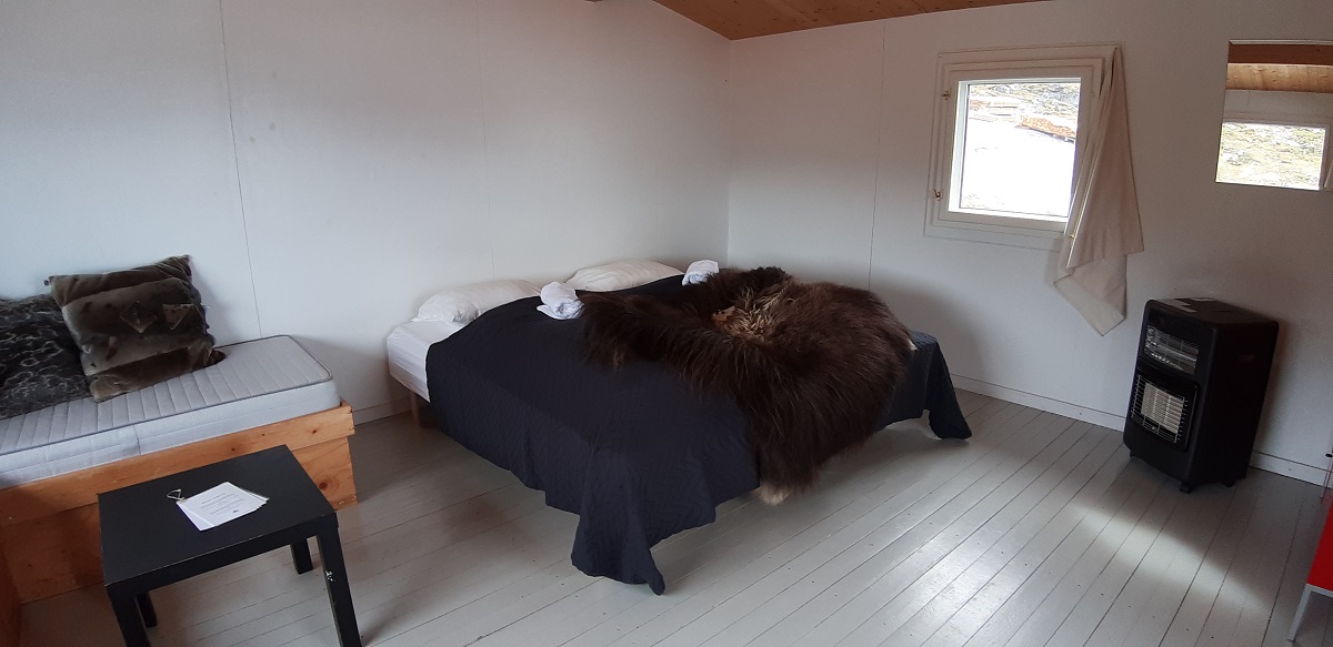 Een bed met zwart tafeltje in de kamer van de standaard hut in Eqi kamp, west Groenland.