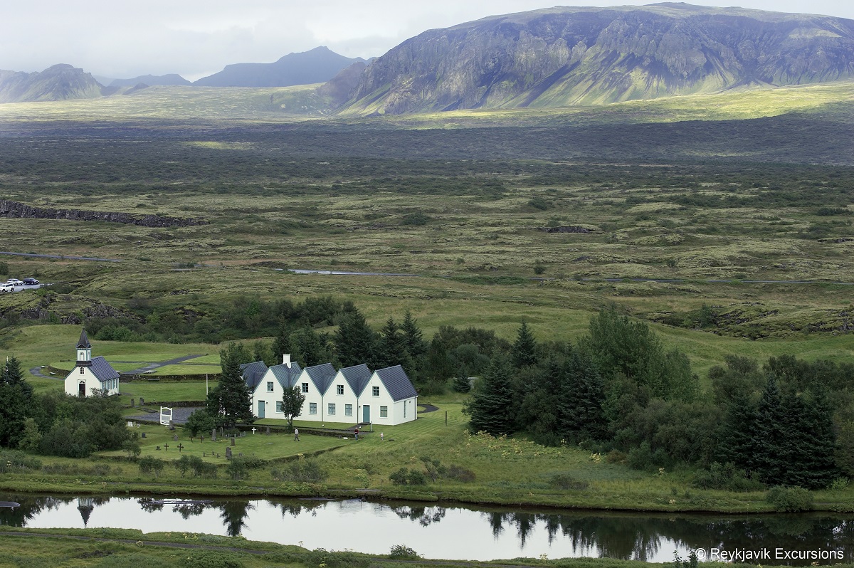 Een witte kerk en huisjes in een mooi groen landschap met de bergen van het NP Thingvellir op de achtergrond.