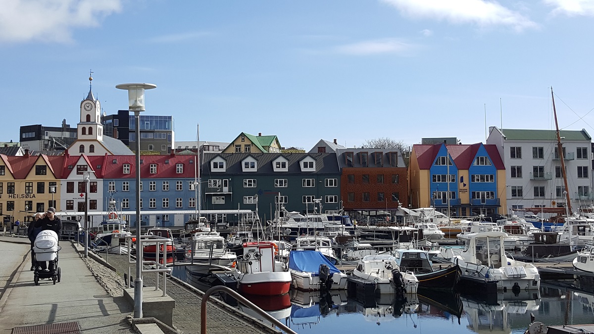 Een stel loopt met een kinderwagen langs de kleurrijke haven van Torshavn, Faroer.