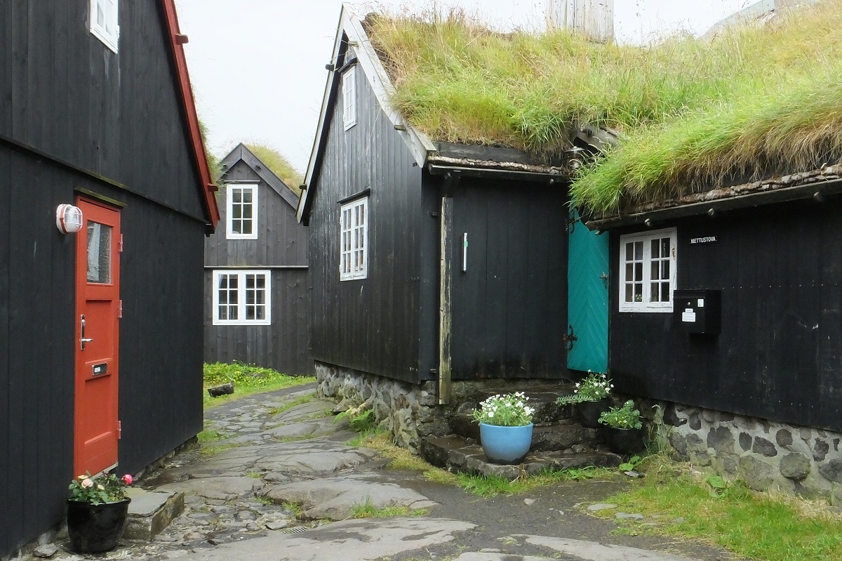 Een smal straatje met kleine zwarte, houten huisjes met grasdaken in Torshavn, Faroer.