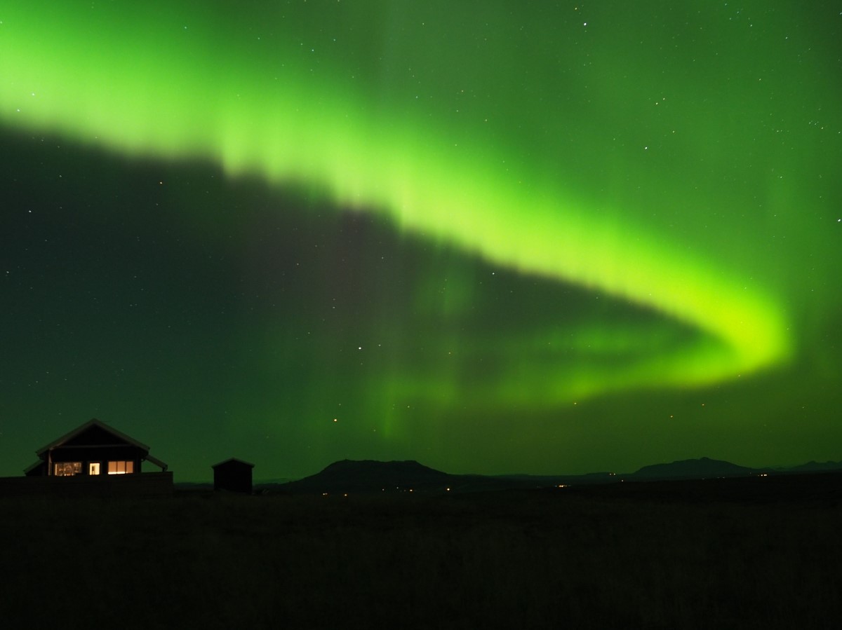 Groen noorderlicht verspreid zich door de lucht vlak boven de vakantiehuisjes van Blue View Cabins.