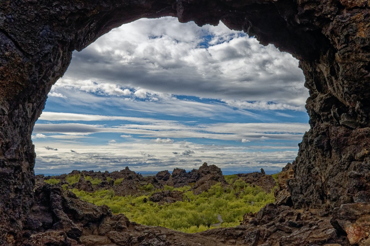 Groene boompjes en een blauwe lucht met wolken maken het uitzicht op Dimmuborgir net een schilderij.