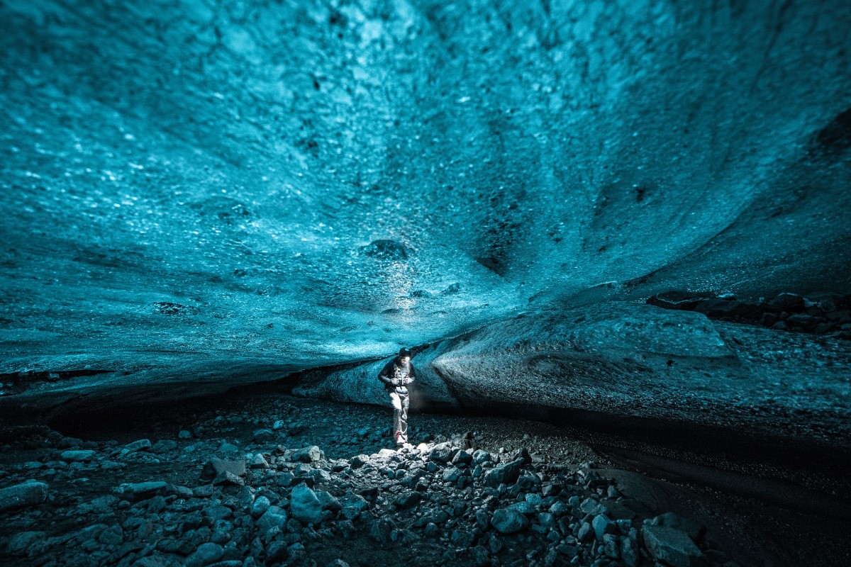Onder het dikke, helderblauw ijs van de gletsjer Vatnajokull, staat een reiziger in de ijsgrot.