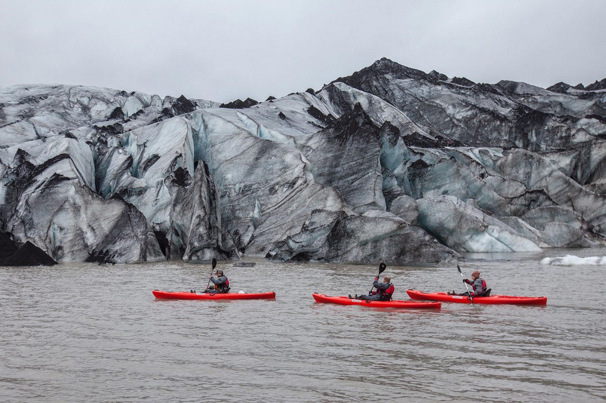 Drie rode kajaks varen langs de rand van de gletsjer Solheimajokull.