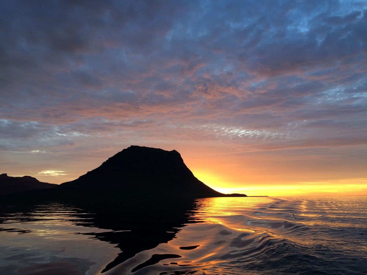 Oranje, roze en blauwe kleuren sieren de lucht tijdens een zonsondergang met de contouren van Kirkjufell op de voorgrond.