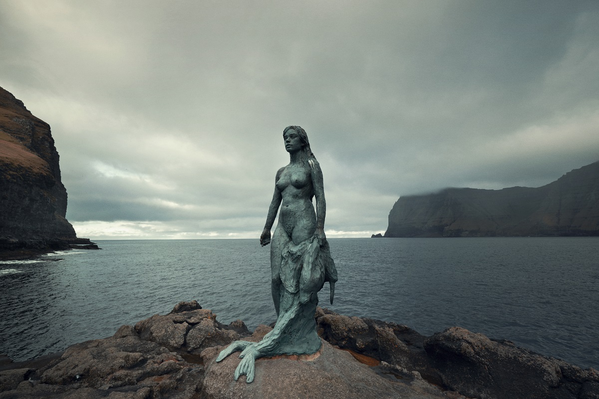 Standbeeld van de zeehondenvrouw aan de randvan het water.