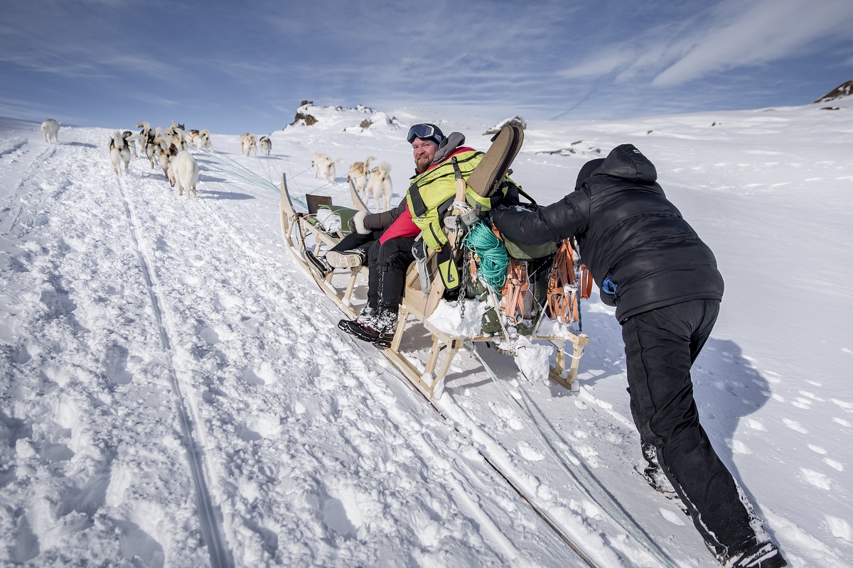 Een musher duwt zijn hondenslee de berg op.