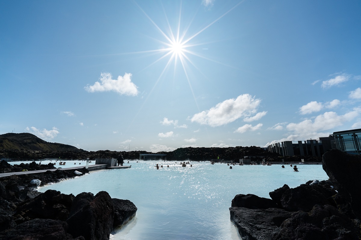 De zon schijnt op de Blue Lagoon, waarin mensen aan het zwemmen zijn. 