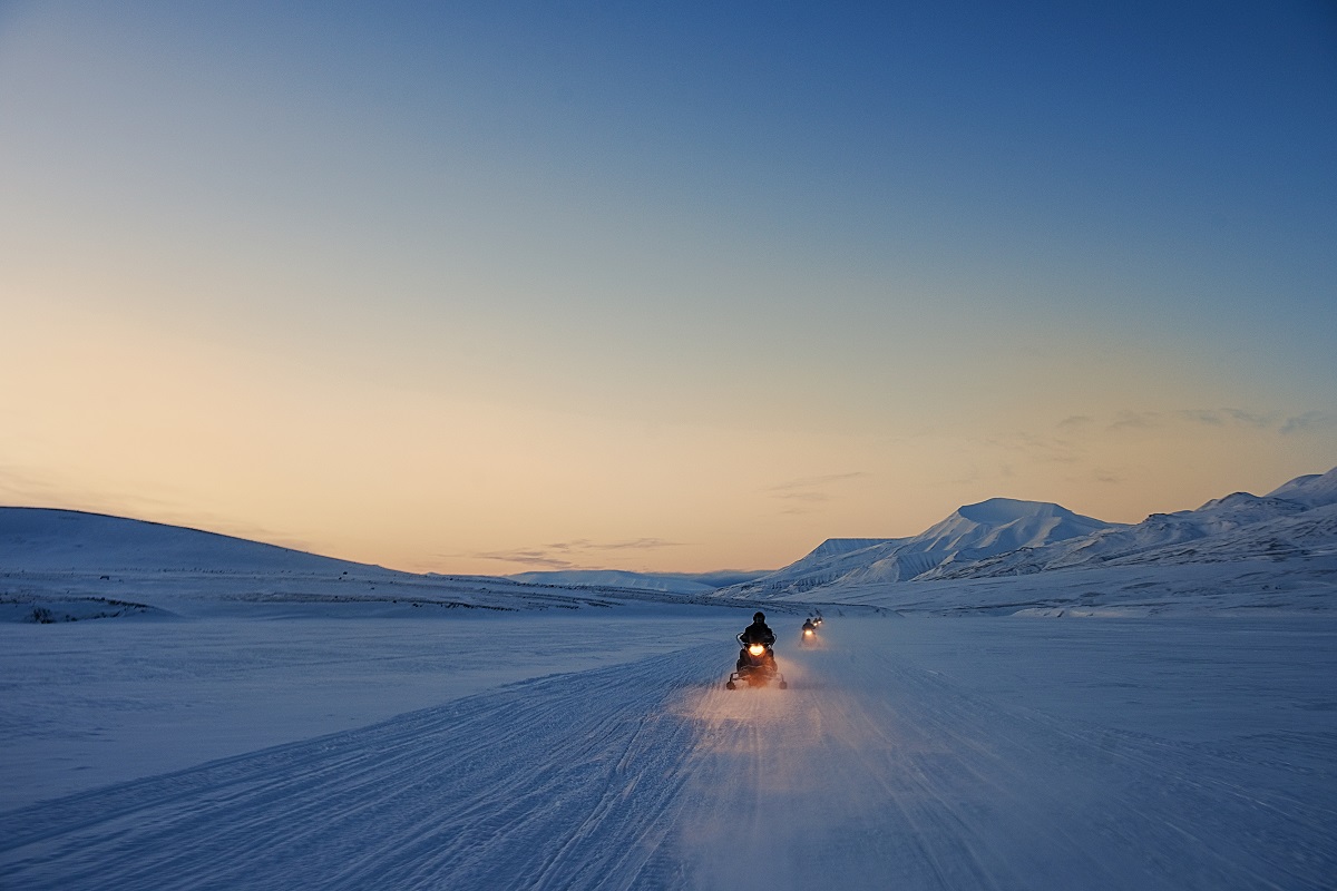 Twee sneeuwscooters rijden door het besneeuwde landscha in de semering op Spitsbergen.