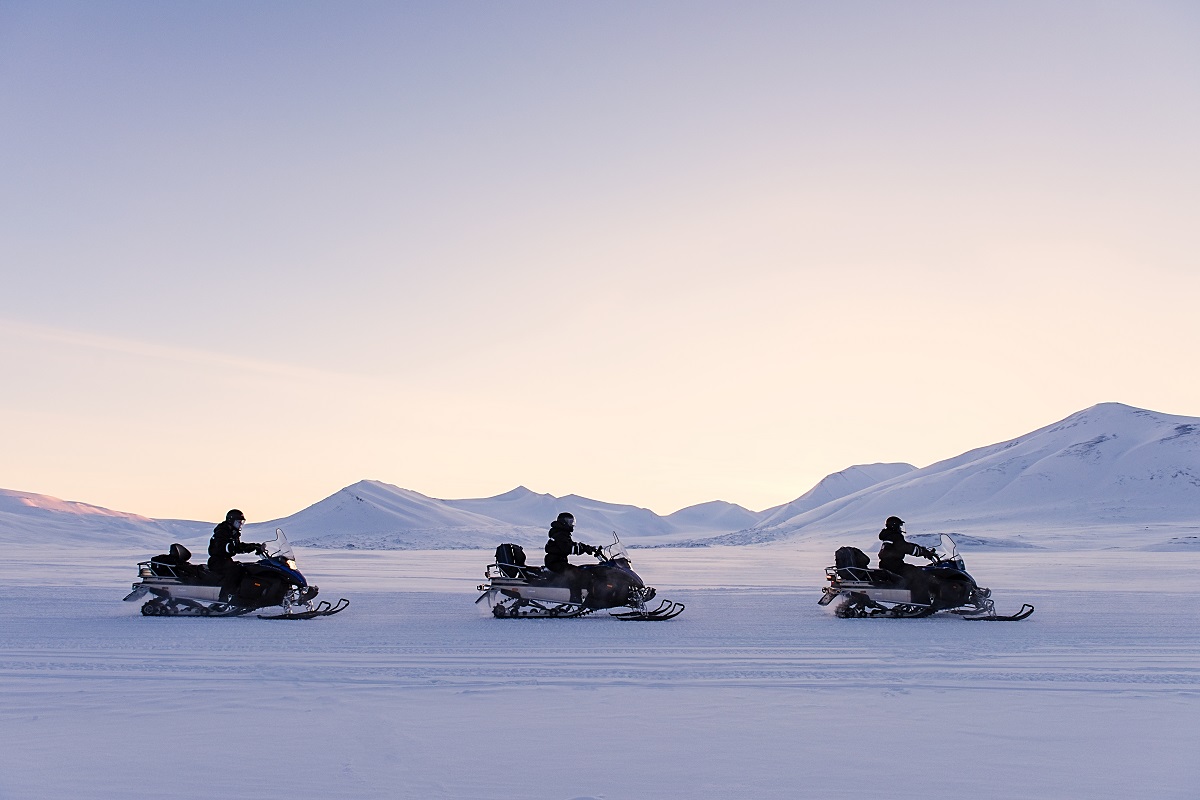 Drie sneeuwscooters bij zondsopgang in het winterse landschap van Spitsbergen.