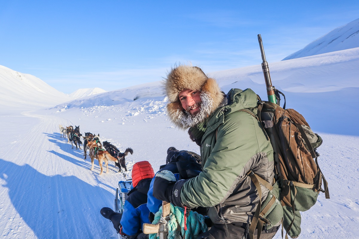 Een dik ingepakte gids met wapen op een hondenslee op Spitsbergen.