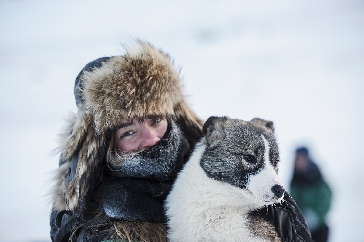 Een dik ingepakte reizigster knuffelt een hond in winters Spitsbergen.