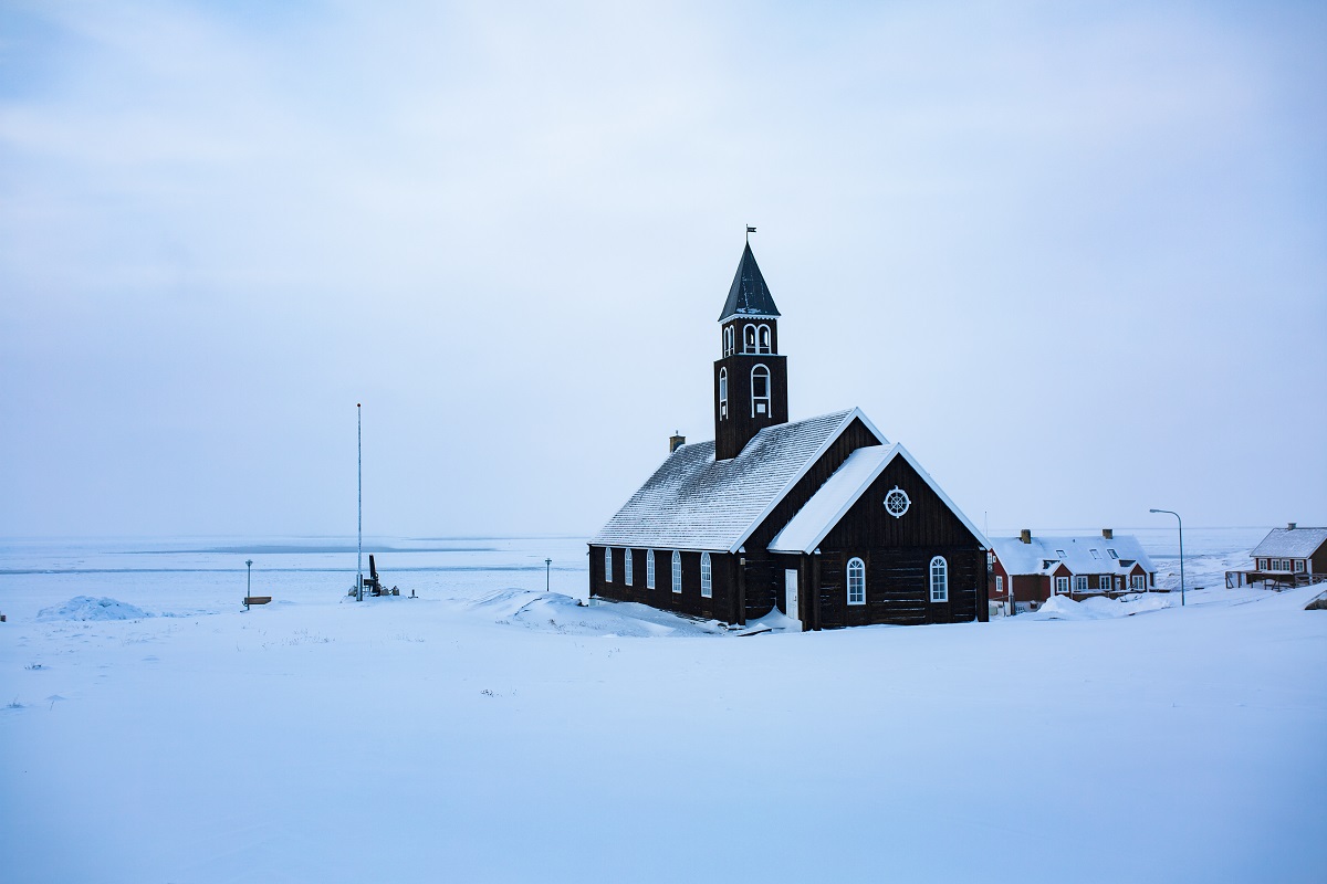 Een zwarte kerk is met sneeuw bedekt en kijkt uit op het fjord in winters Ilulissat, gelegen in het westen van Groenland.