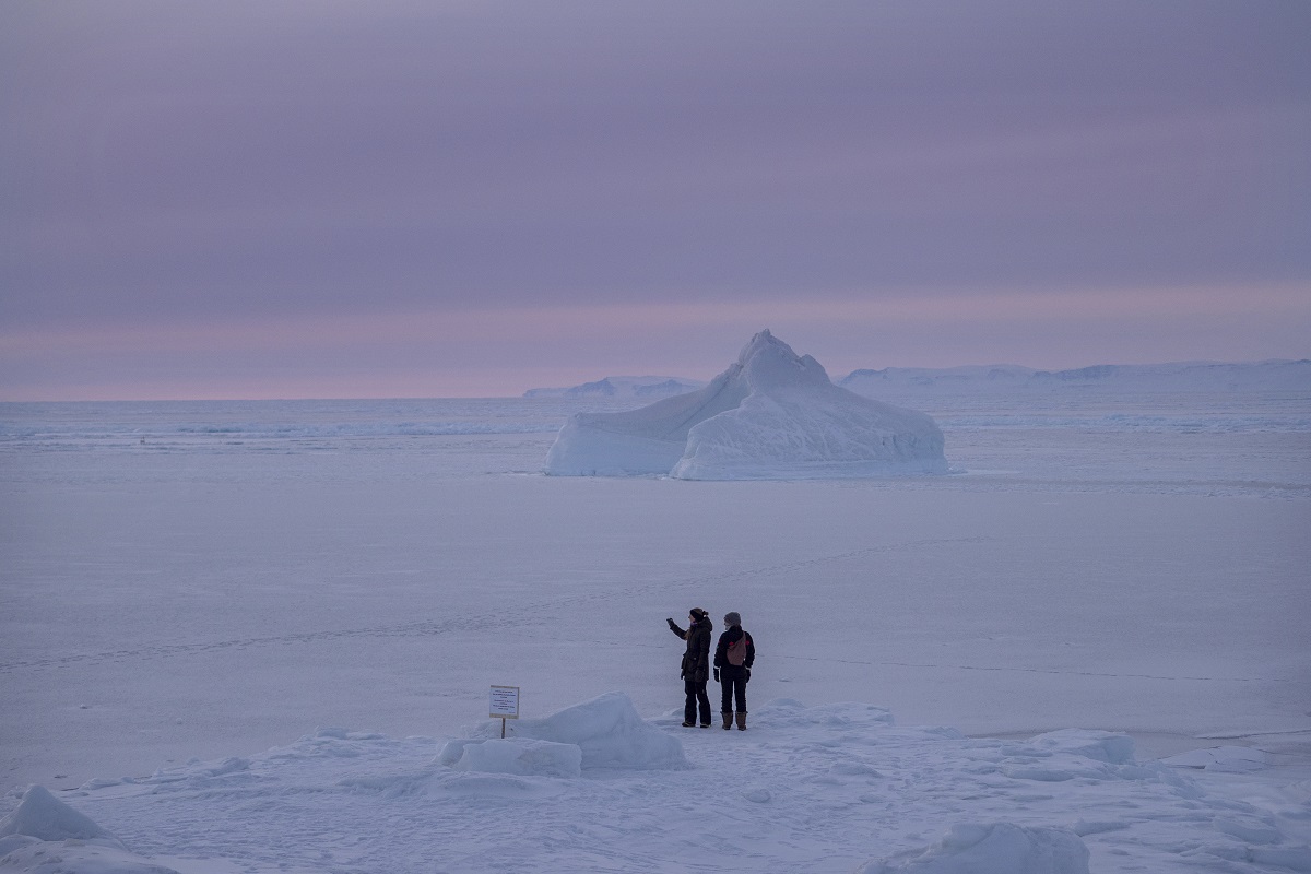 Twee reizigers kijken naar een uitzichtpunt op het bevroren en besneeuwde fjord in Ilulissat in de winter.