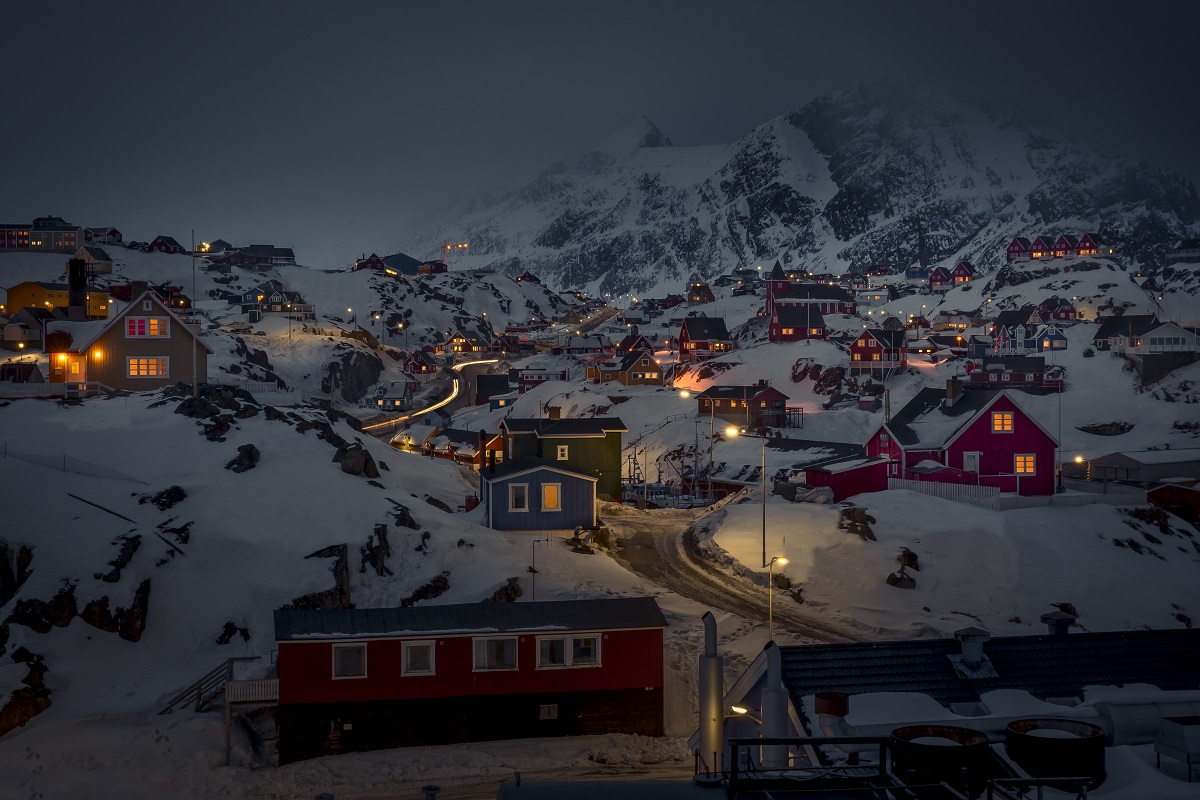 De lichtjes branden in de huizen in Sisimiut in de winter in West-Groenland. De daken zijn bedekt met sneeuw en het is nacht.