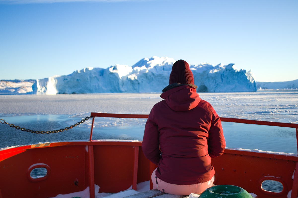 Een reiziger zit op een boot tijdens een excursie op het Ilulissat ijsfjord met op de achtergrond grote ijsbergen. De zon schijnt in de winter, in west Groenland.