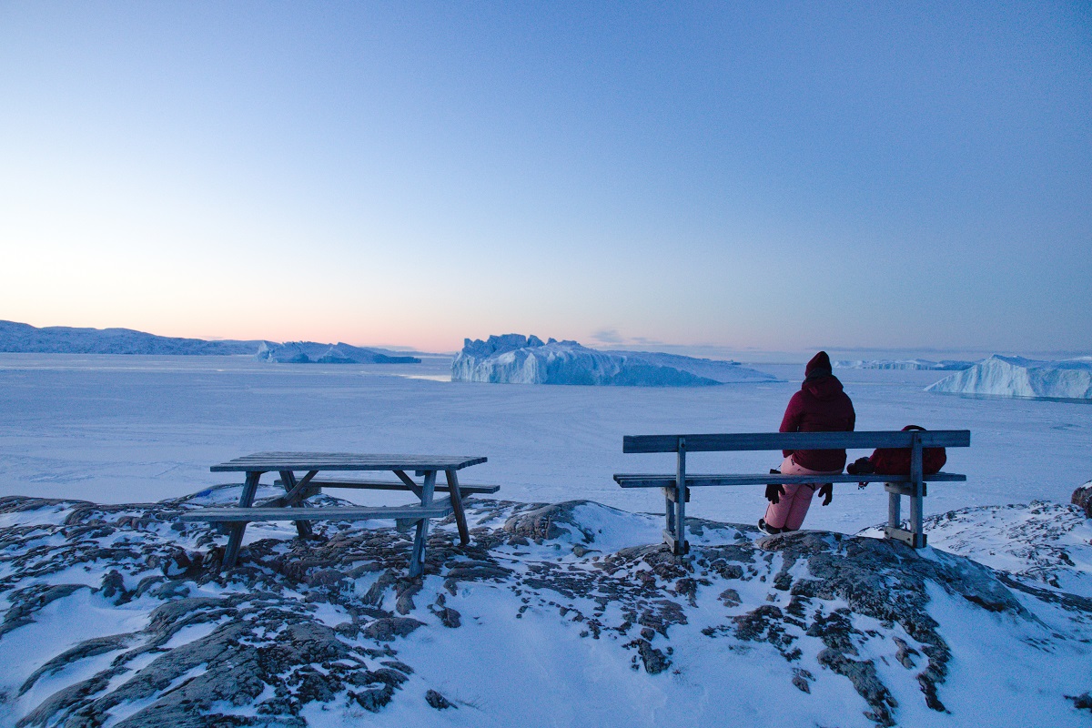 Reiziger bij de zonsopkomst over het Kangia ijsfjord in Ilulissat, West-Groenland. Het winterlandschap is bedekt met een dikke laag sneeuw en de lucht is helder.