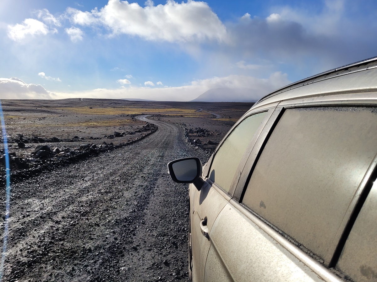 Op de Kjolur hooglandenroute zit een auto onder het zand en stof op een gravelweg.