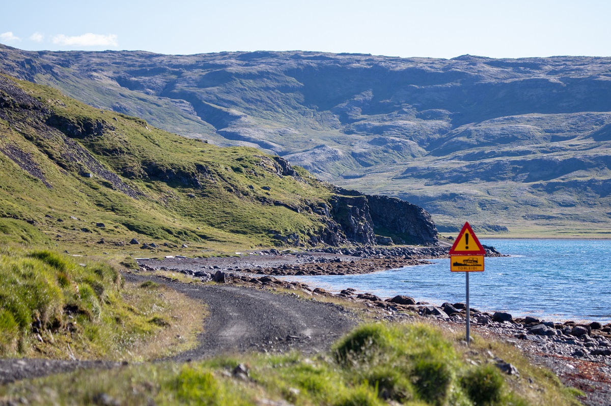 Een weg met een waarschuwingsbord langs de Strandir kustlijn. Bij het Ingolfsfjordur fjord gelegen in de Westfjorden.