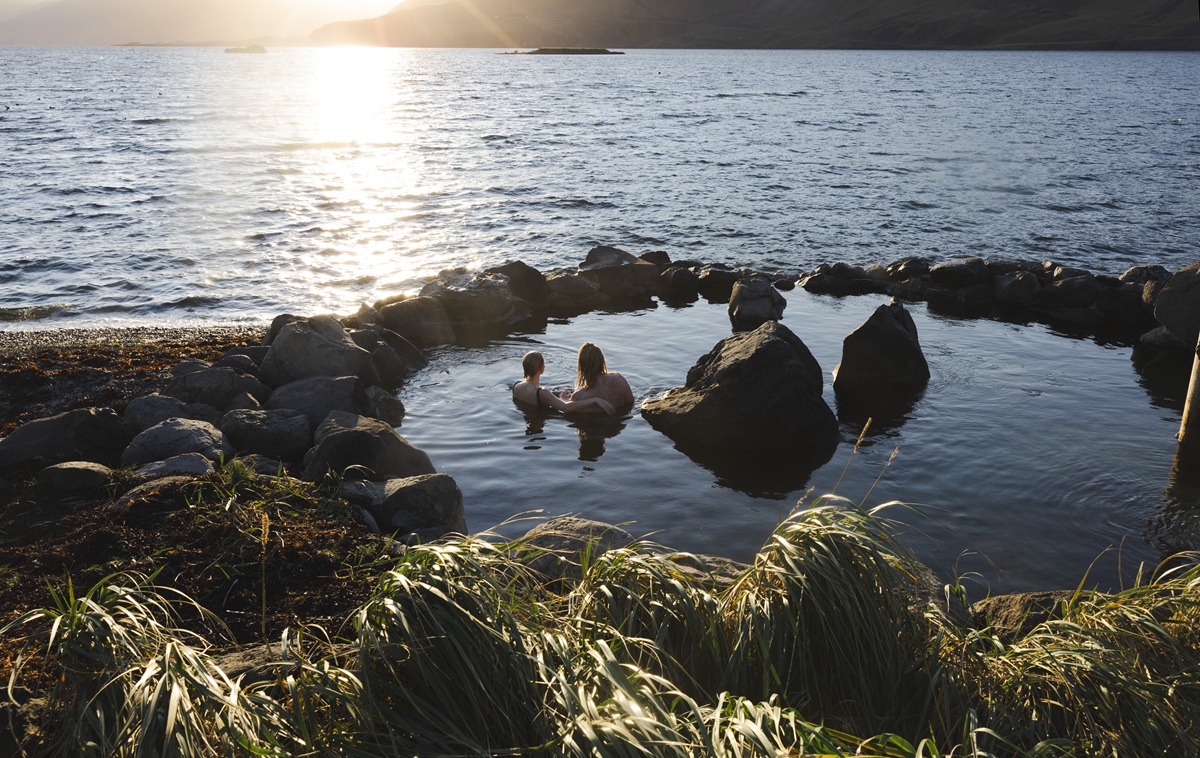 Twee reizigers zitten bij zonsondergang in Hvammsvik Baths.